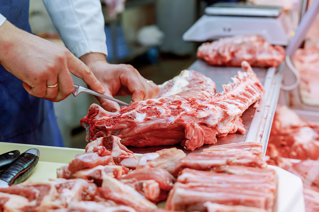 Cropped image of male butcher cutting raw meat with knife at counter shop